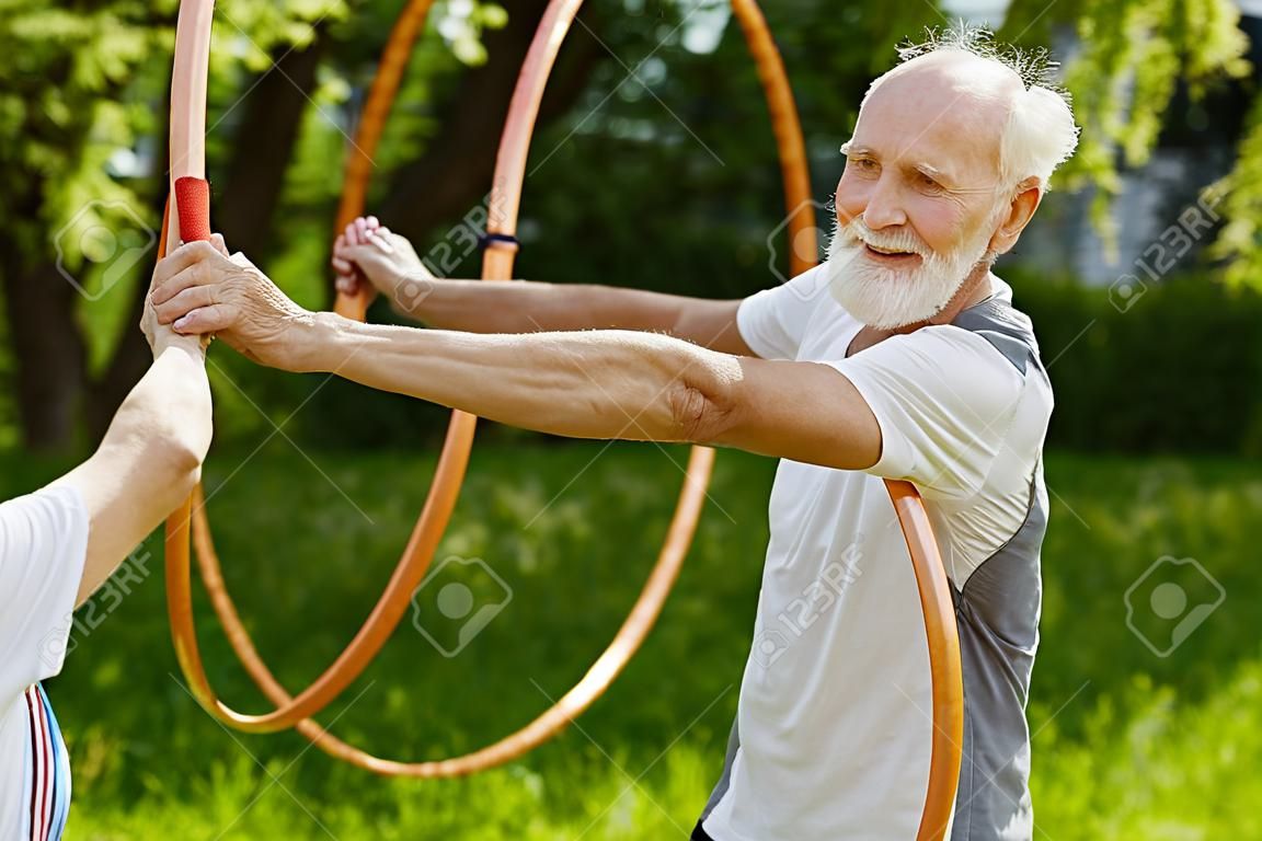 Glückliche ältere Menschen, die Sport mit Reifen in einem Sommergarten