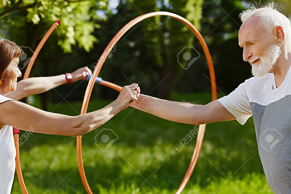 Happy persone anziane che fanno sport con cerchi in un giardino estivo