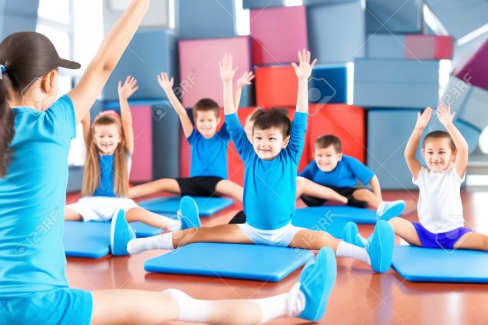 Groupe d'enfants qui font des enfants dans le gymnase de gymnastique avec puéricultrice