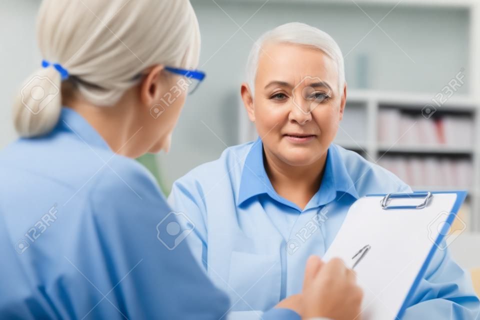 클립보드가 있는 여성 의사는 기억 상실증의 환자로 노인을 인터뷰합니다.