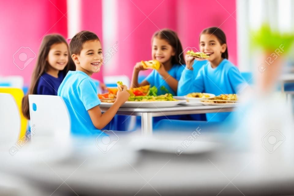 学校の食堂で昼食を食べる友人としての子供たちのグループ