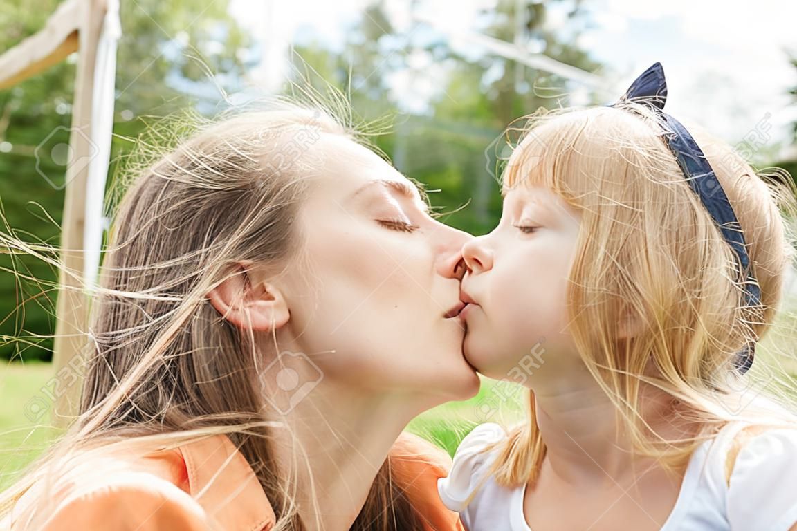 Mutter und Tochter küssen sich liebevoll im Garten mit geschlossenen Augen