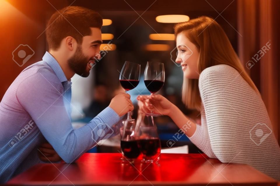 Zakochana młoda para spotyka się w restauracji, pijąc kieliszek czerwonego wina