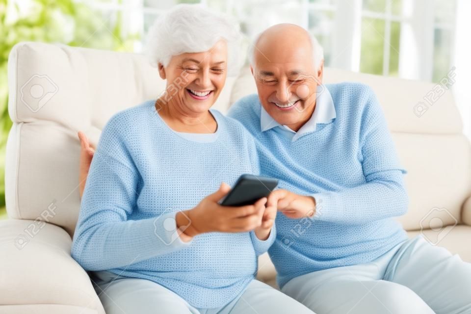스마트폰을 사용하는 노인 부부는 재미있는 비디오 채팅을 하거나 문자 메시지를 읽습니다.
