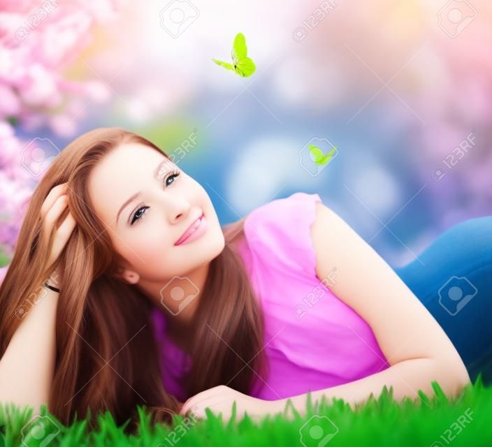 春季美容美麗的女孩躺在綠色的草地上戶外