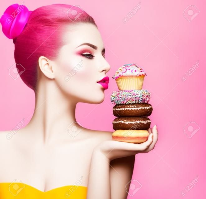 美女时尚模特女孩拿糖果和七彩甜甜圈