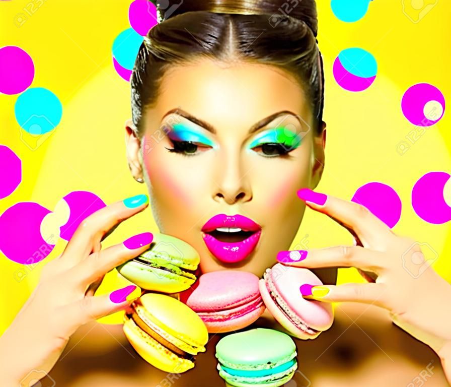 Beauty fashion model girl with colourful makeup taking colorful macaroons
