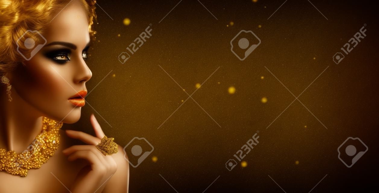 Mujer de oro. Chica de modelo de moda de belleza con maquillaje dorado, cabello y joyas sobre fondo negro