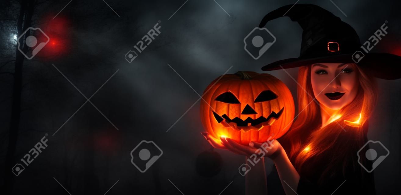 Halloween Hexe mit einem geschnitzten Kürbis und magische Lichter in einem dunklen Wald