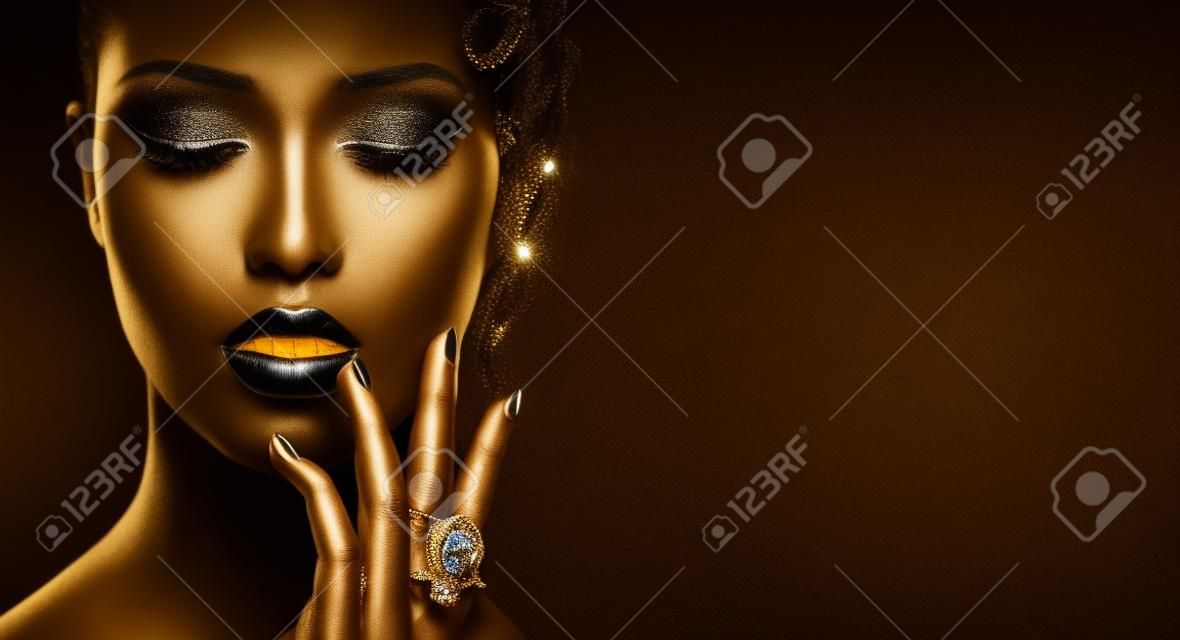 Fashion model with black skin, golden lips, eyelashes and jewellery - golden ring on hand. Isolated on black background. Beauty woman face, beautiful make-up. Gorgeous lady fashion art portrait
