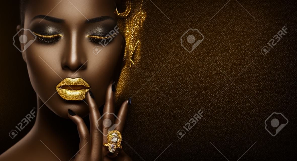 Modelka z czarną skórą, złotymi ustami, rzęsami i biżuterią - złoty pierścionek na dłoni. Na białym tle na czarnym tle. Piękna twarz kobiety, piękny makijaż. Wspaniały portret sztuki mody damy