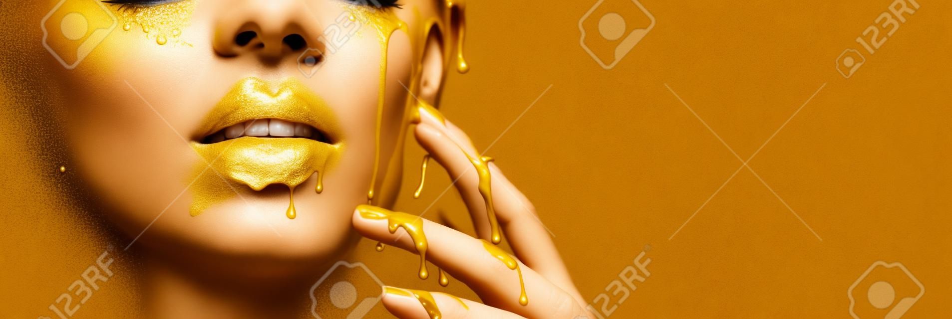 Manchas de tinta dourada goteja dos lábios do rosto e da mão, gotas líquidas douradas na boca da menina modelo bonita, maquiagem abstrata criativa.