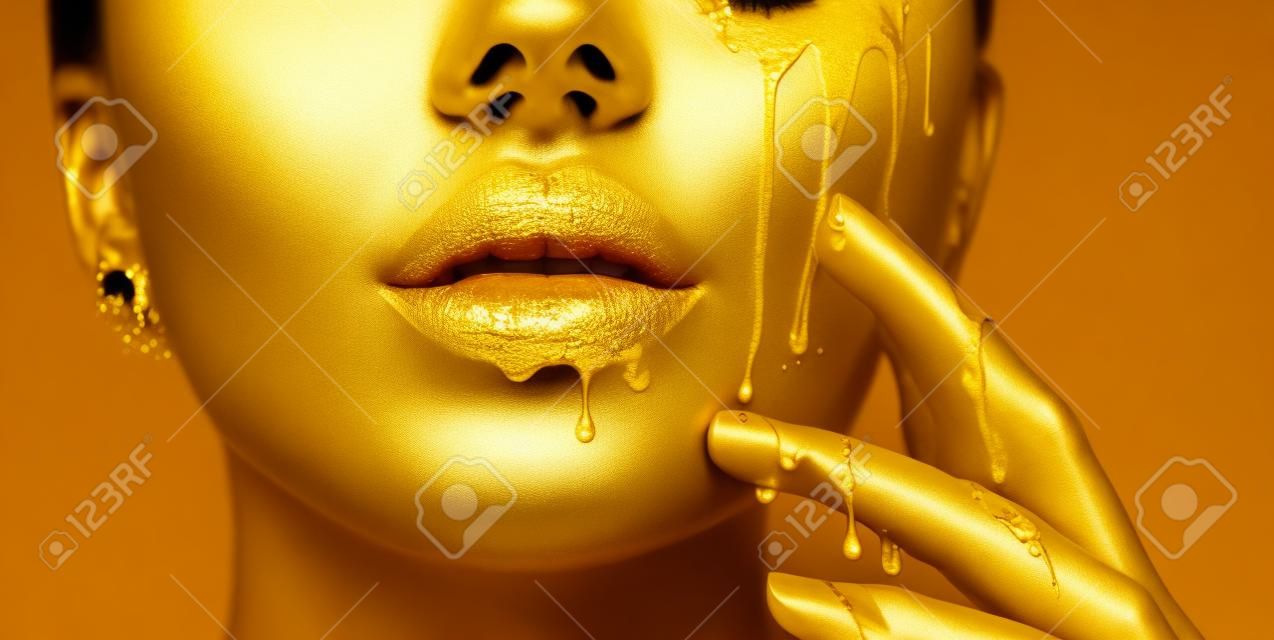 Manchas de pintura dorada gotean de los labios de la cara y la mano, gotas de líquido dorado en la boca de la chica hermosa modelo, maquillaje abstracto creativo. Rostro de mujer de belleza