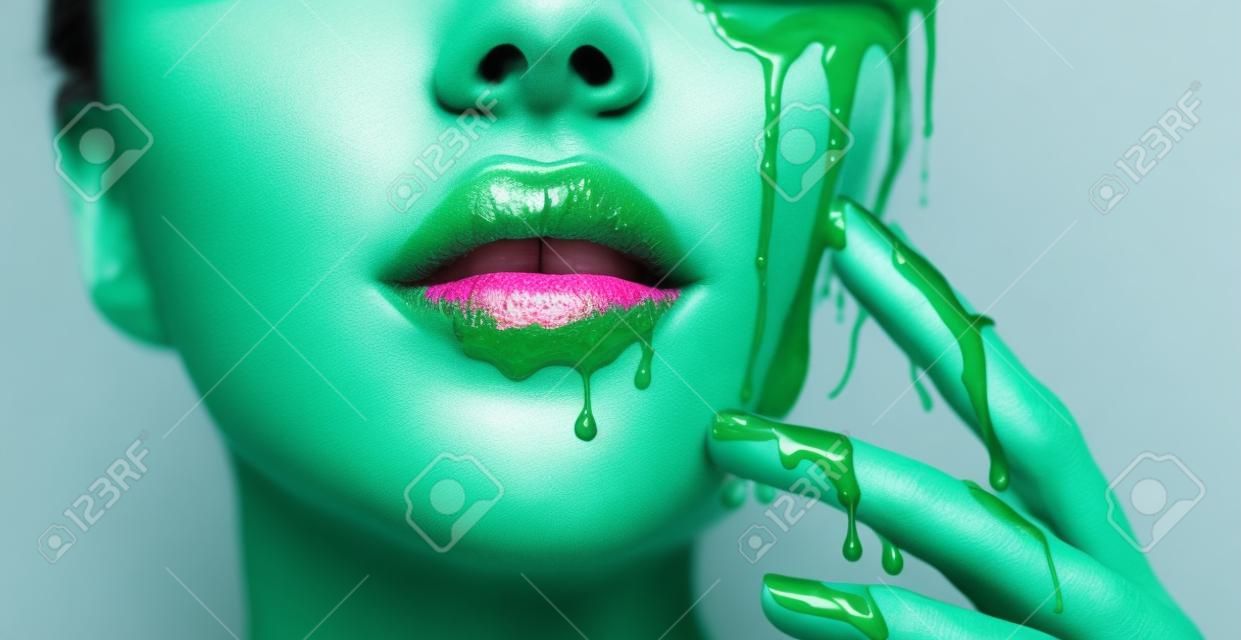 Smugi kapie z ust i dłoni, zielony płyn spada na usta pięknej modelki, kreatywny abstrakcyjny makijaż. piękna twarz kobiety