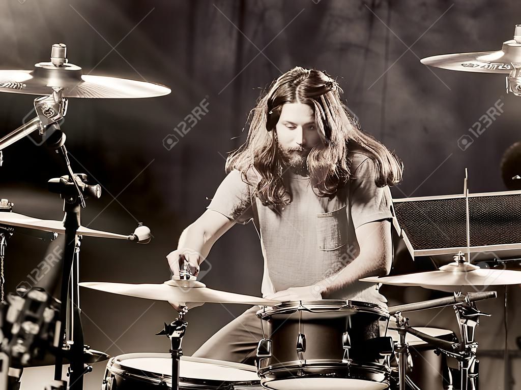 Foto van een jonge mannelijke drummer met lang haar die zijn drumstel speelt.