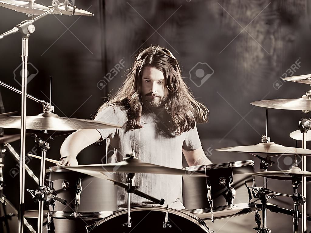 Фотография молодого барабанщика-мужчины с длинными волосами, играющего на барабане.