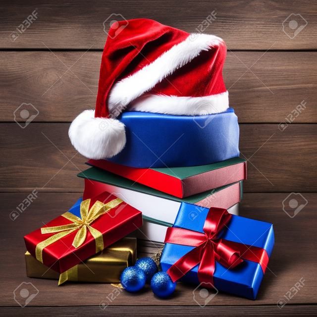 Una pila di libri, cappello di Babbo Natale, scatole regalo con nastri rossi e blu su fondo di legno. Concetto di nuovo anno e buon Natale