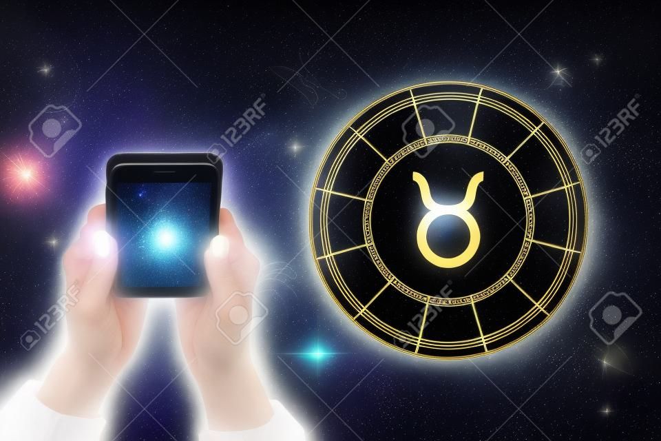 Weibliche Hände halten ein Telefon und einen astrologischen Kreis mit dem Sternzeichen Stier vor dem Hintergrund des Sternenhimmels. Horoskop-App.