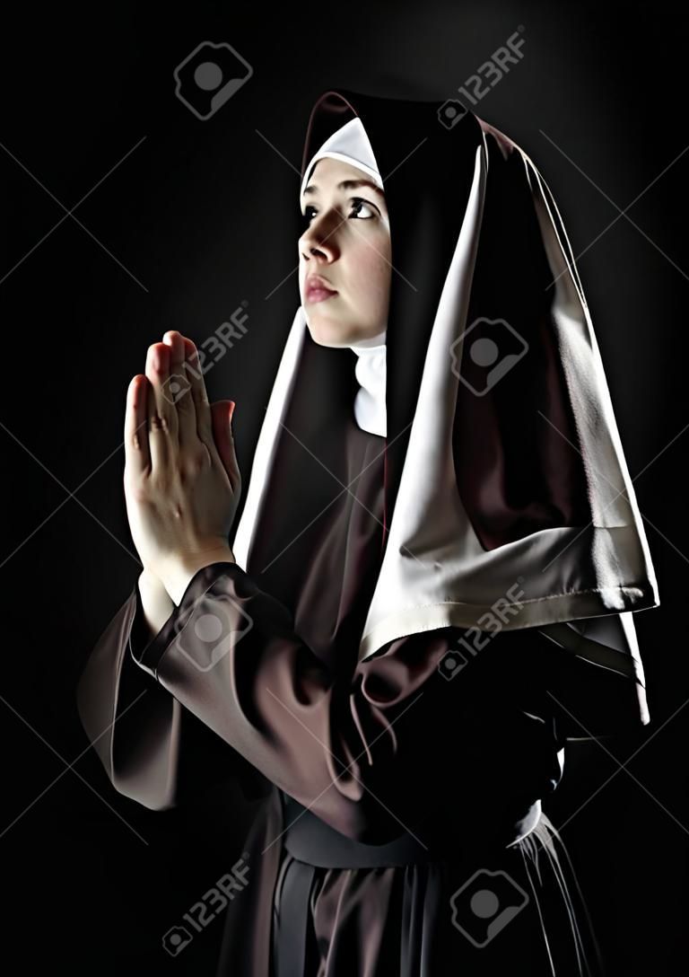 Giovane suora cattolica di pregare. Foto su sfondo nero.