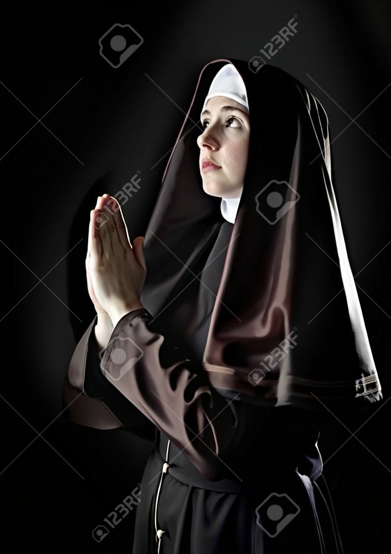 Giovane suora cattolica di pregare. Foto su sfondo nero.
