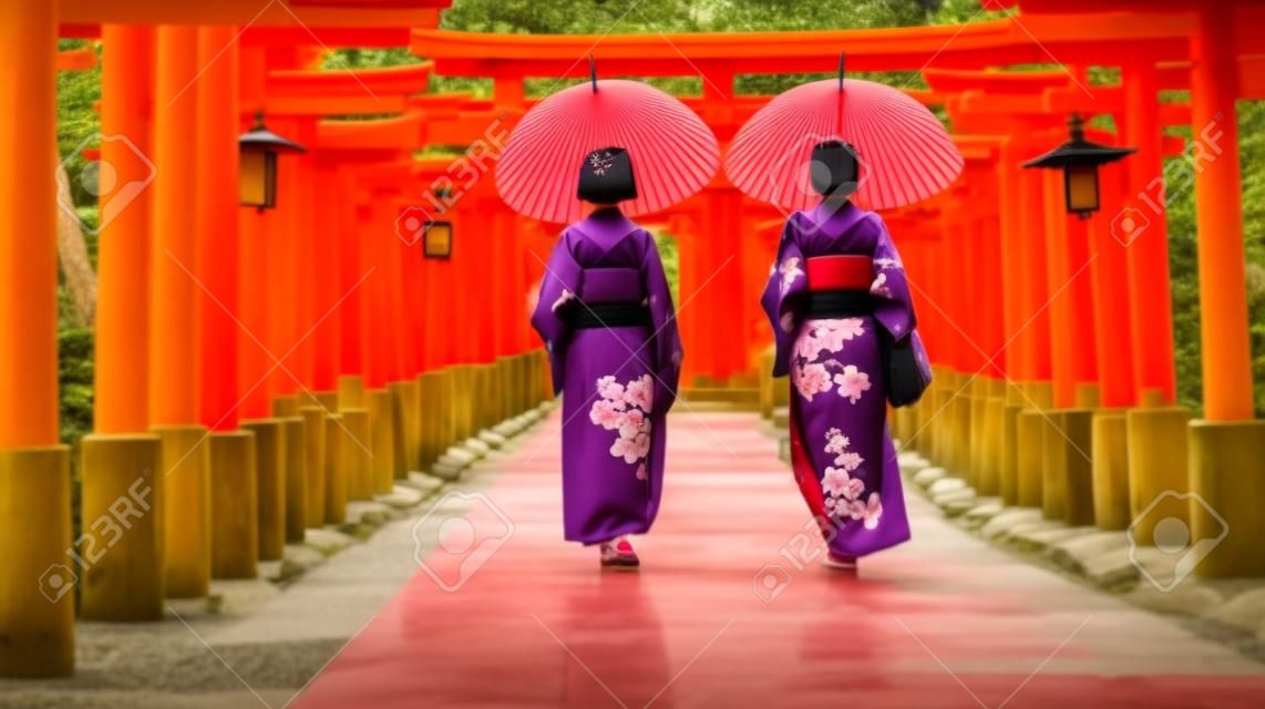 Backside two women in traditional kimono and umbrellas walking at Torii gates, Japan