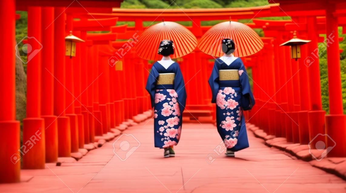 Backside two women in traditional kimono and umbrellas walking at Torii gates, Japan
