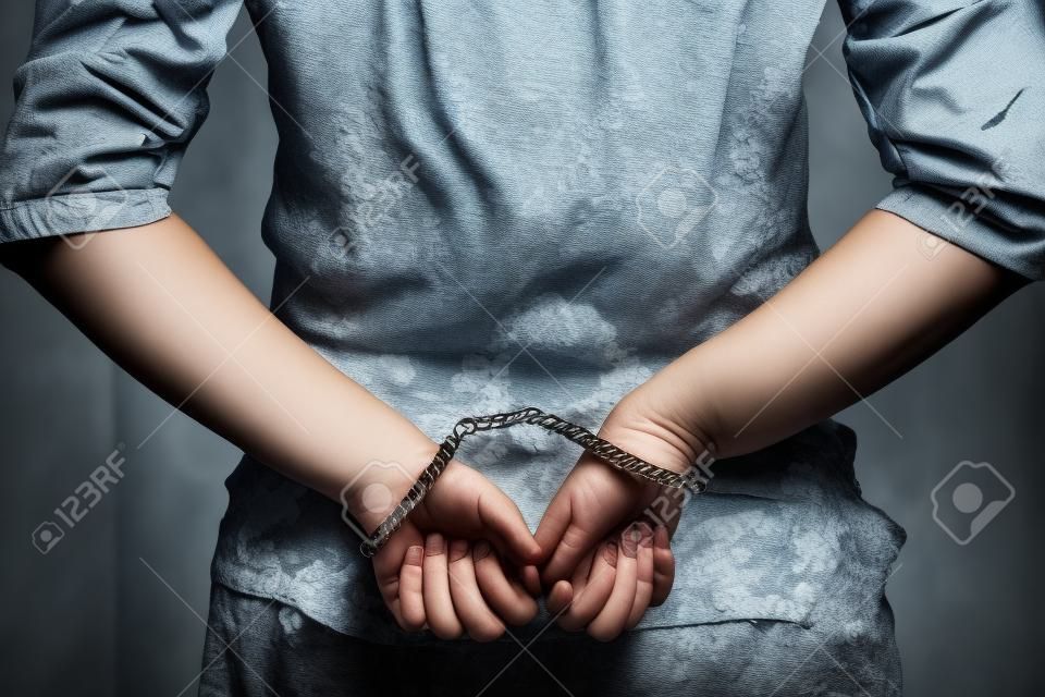 Mujer arrestada esposada con las manos en la espalda. Prisionero o terrorista arrestado, pirata informático, soborno, primer plano de las manos esposadas. De cerca. Viraje