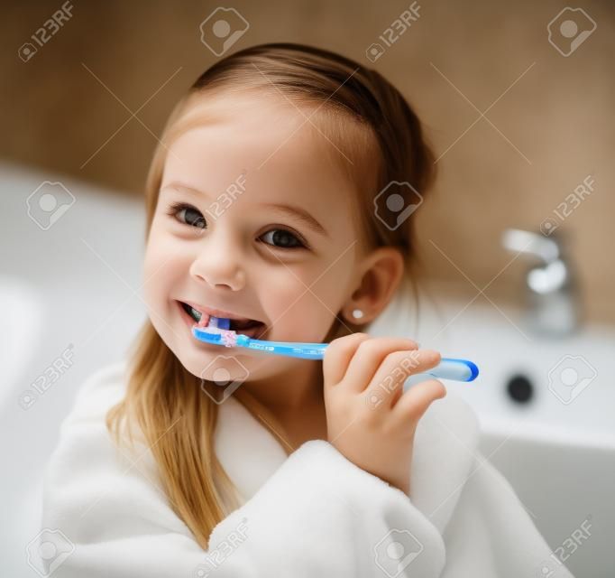 Smiling little girl brushing teeth in bath 