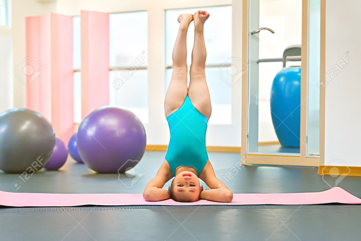 Flexible petite fille gymnaste debout sur la tête dans une salle de sport. Sport, formation, fitness, yoga, concept de style de vie actif