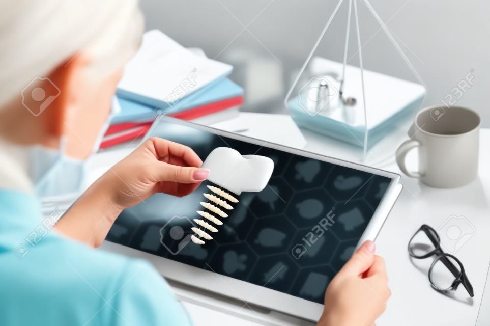 Kobieta z laptopem na jej biurku. trzyma ikonę implantu zębów. szukaj dentystów, usługi dentystyczne, konsultacje.