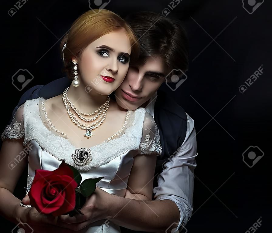 복고 스타일의 아름 다운 커플입니다. 남자가 여자를 안아줍니다. 남자의 배경에 빨간 장미와 흰 드레스에 아름 다운 소녀.