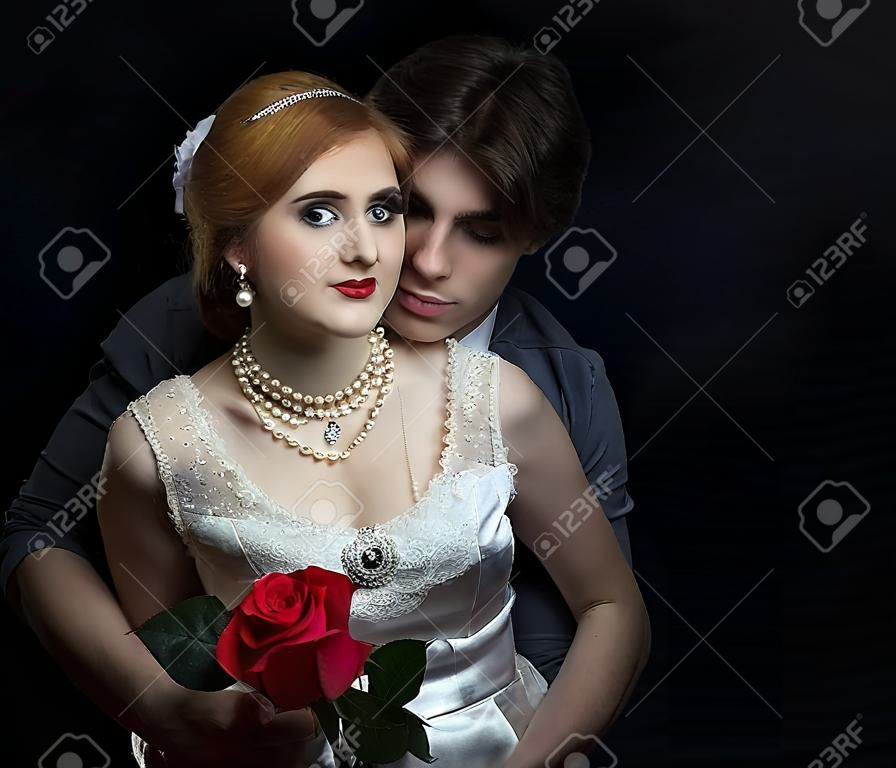 복고 스타일의 아름 다운 커플입니다. 남자가 여자를 안아줍니다. 남자의 배경에 빨간 장미와 흰 드레스에 아름 다운 소녀.