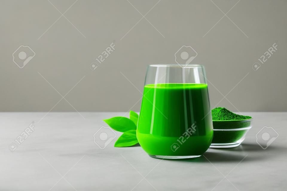 Chlorella healthy detox drink in glass and powder in bowl on a gray background. Close up. Space for design.