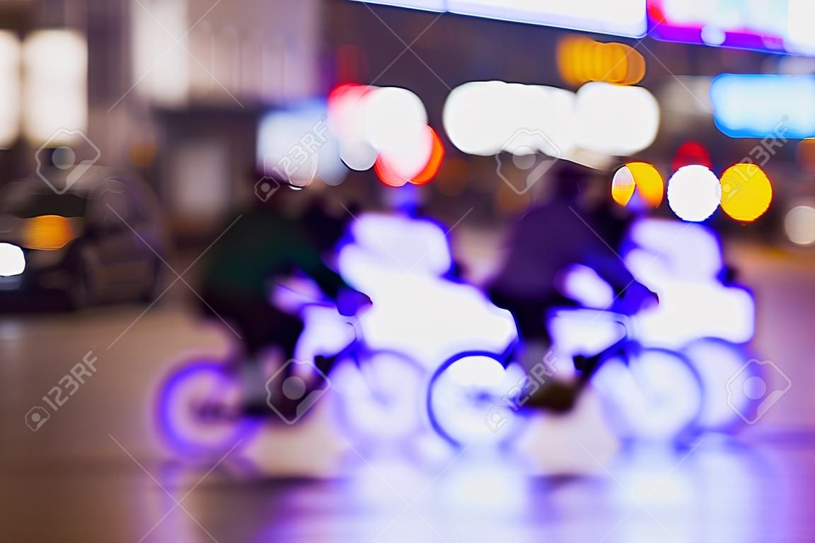 Silhuetas de ciclistas de equitação no trânsito na cidade da noite, bokeh leve, abstrato, motion blur, fundo violeta