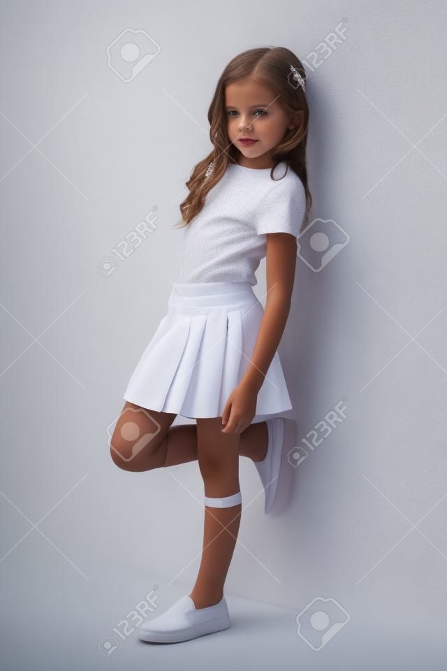 Piękne dziewczynka w spódnicy stojących koło białej ścianie i stwarzających jak modelu