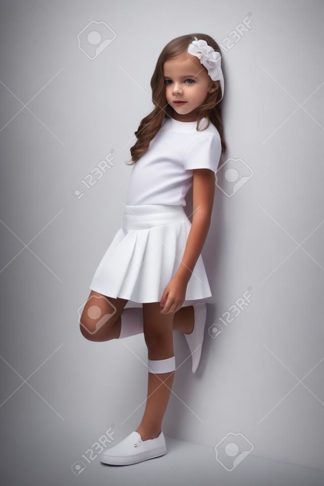 Piękne dziewczynka w spódnicy stojących koło białej ścianie i stwarzających jak modelu