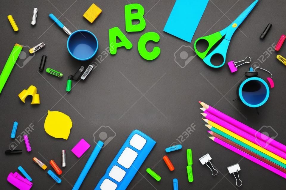 In tsetre black background blank space for text, mock up. Bright colored school and office supplies are arranged around.