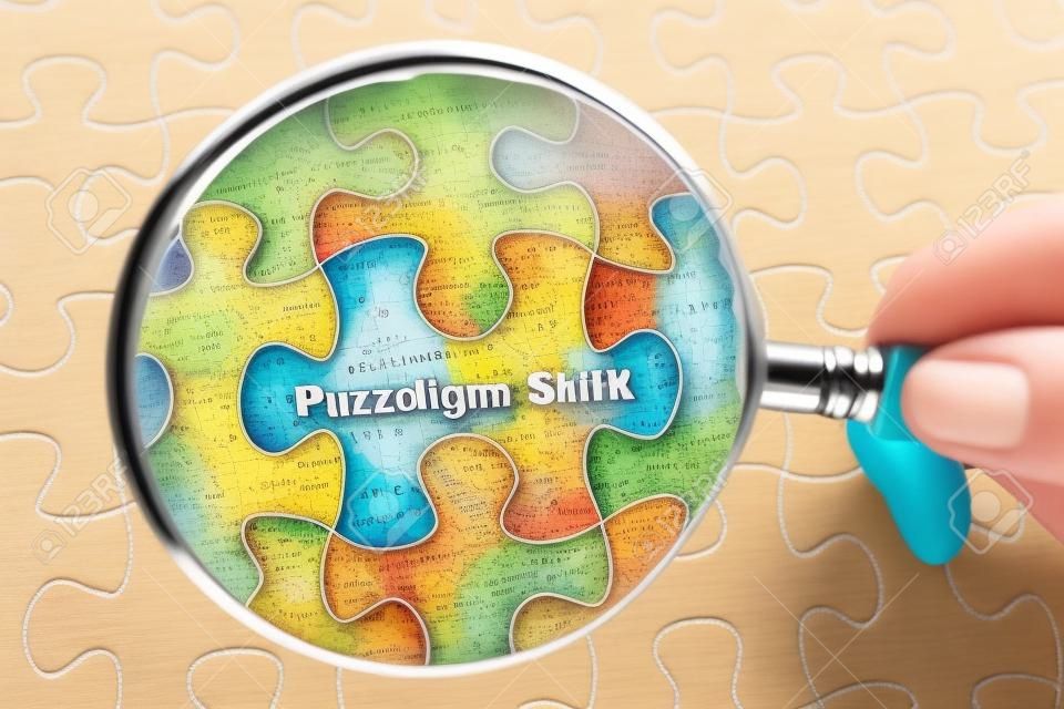 Hand holding magnifying glass over jigsaw puzzle with word Paradigm Shift