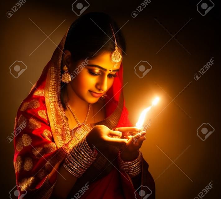 Hermosa joven india en sari vestimenta tradicional de la celebración de una lámpara de aceite Diwali, aislado sobre fondo negro.