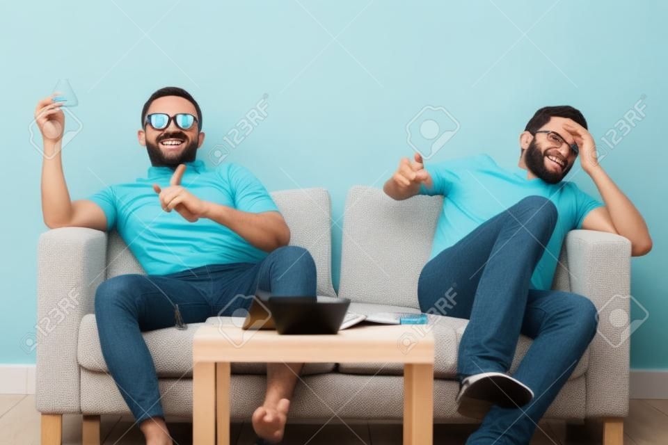 Group of men sitting on sofa watching live sport together at home.