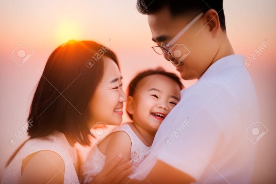 Lovely Asian family outdoor portrait, enjoying holiday together on seaside in beautiful sunset during vacations.