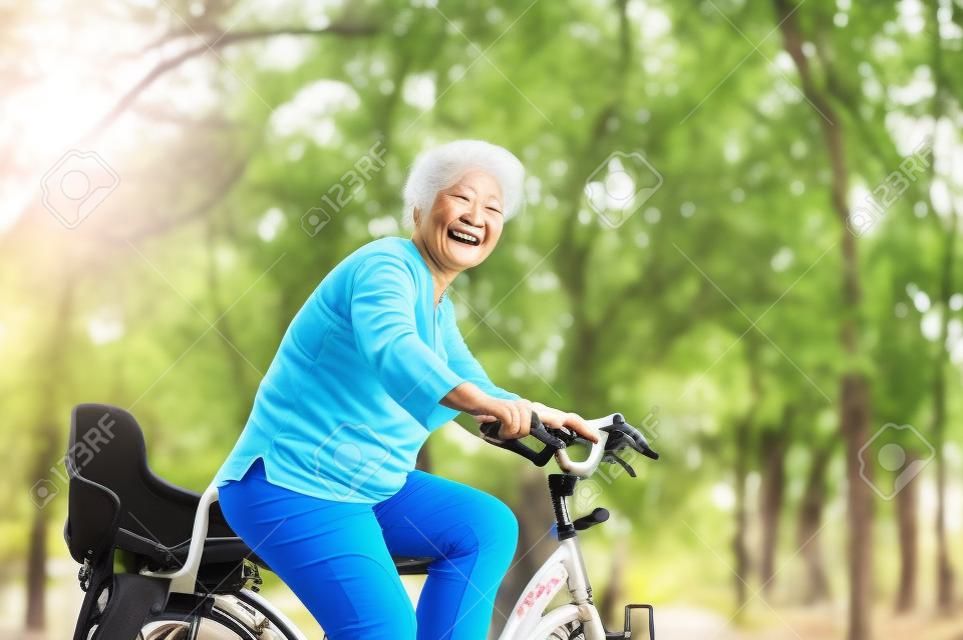 Aktive ältere Asiatin, die, ältere erwachsene Tätigkeit radfährt, Fahrrad reiten, das am Morgen im Freien ist.