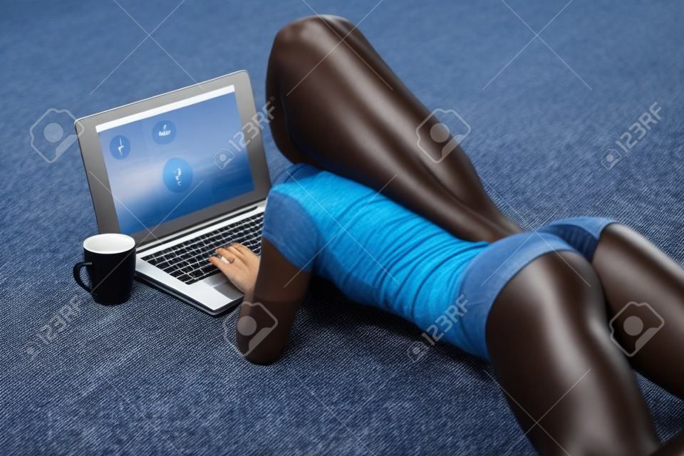 Girl with perfect booty in jeans small shorts working with laptop on carpet at home.