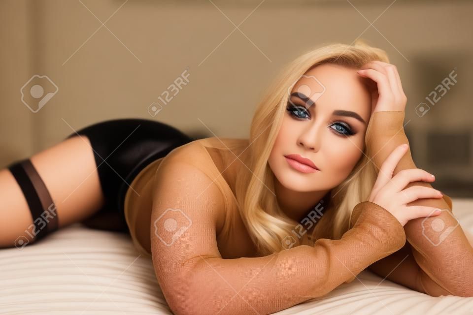 Красивая белокурая женщина представляя на кровати в черном колготки - близком поднимающем вверх портрете красоты.