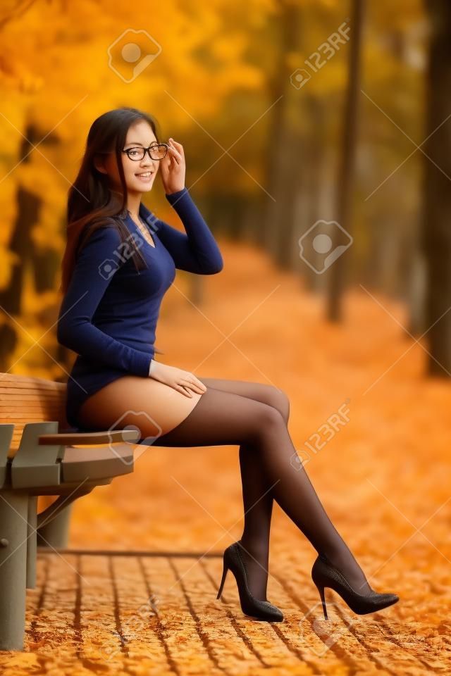 Piękna studentka z idealnymi nogami siedząc na ławce w jesiennym parku.