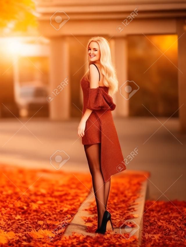 Belle femme blonde avec des jambes parfaites en collants posant en plein air dans la rue d'automne aux lumières du soleil couchant.