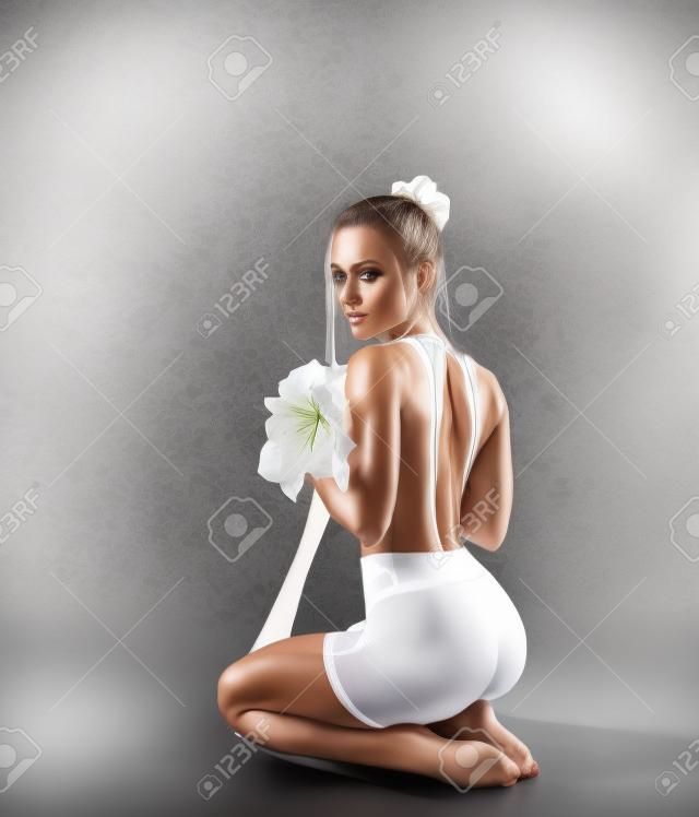 Schöne Fitnessfrau mit perfekten Beinen in weißer Netzstrumpfhose und mit Amaryllis-Blumen - Modestil auf dem Studiohintergrund.
