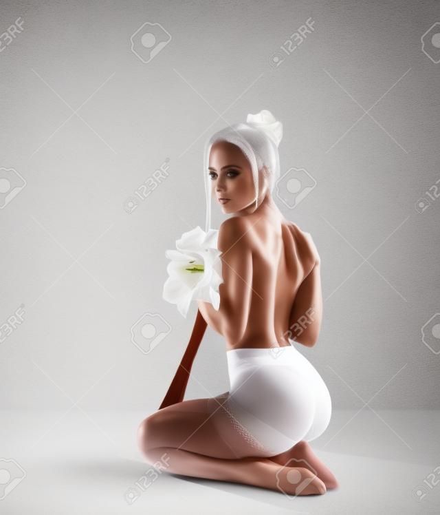 Hermosa mujer fitness con piernas perfectas en pantimedias de rejilla blanca y con flores Amaryllis - estilo de moda en el fondo del estudio.
