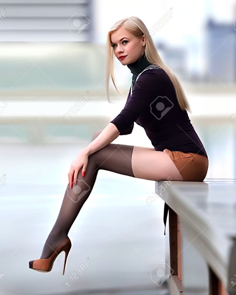 Bella ragazza bionda con gambe perfette in collant in posa all'aperto sulla strada della città.