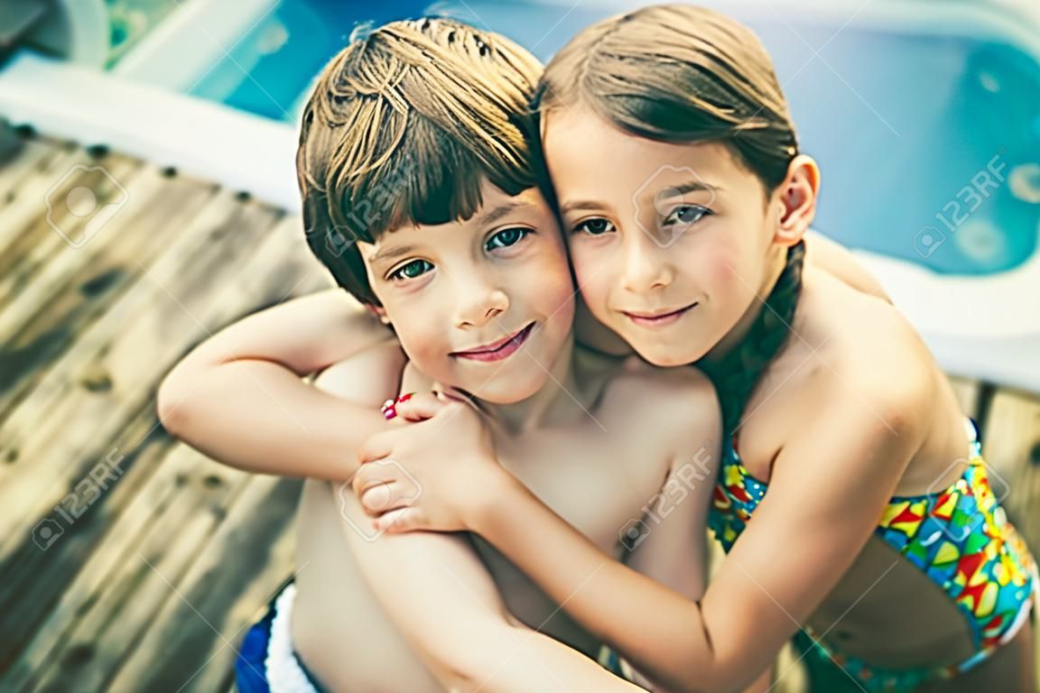 Hermano y hermana abrazos en traje de baño en frente de un jacuzzi